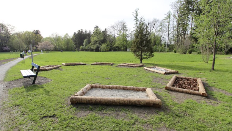 Ein Stadtpark mit einem Barfußpfad aus verschiedenen Materialien und einer Parkbank.