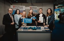 Sechs Personen mit dem Schild Wiener Alpen in Niederösterreich bei einem Prospektpult vom Hilton Garden Inn 