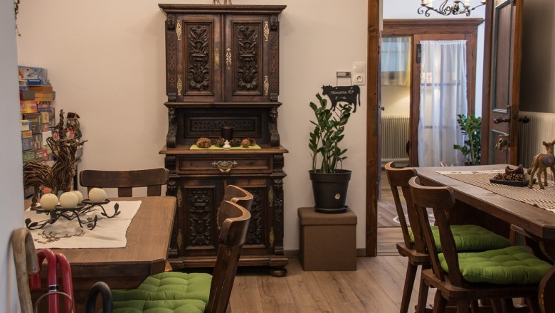 Gemütlicher Aufenthaltsraum mit Holzmöbeln, grünen Sitzkissen und dekorativem Schrank.