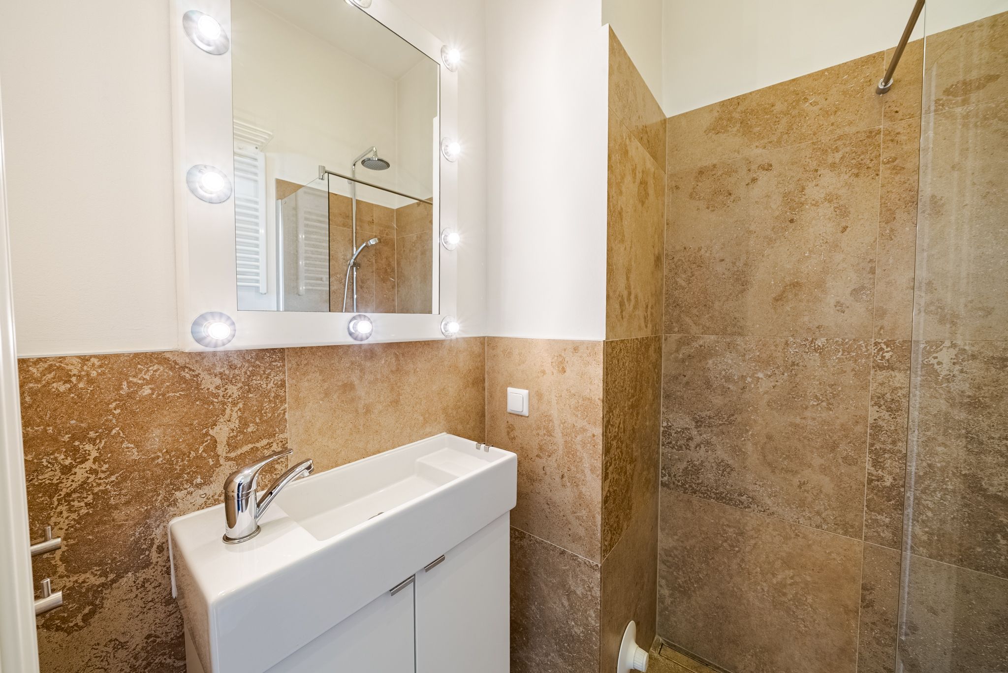 Modernes Badezimmer mit beleuchtetem Spiegel und beiger Fliesenwand.
