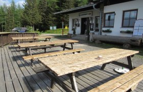 Holzbänke vor der Almrauschhütte in einem Waldgebiet.