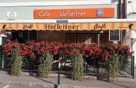 Außenansicht des Café Hofleitner mit roten Blumen und Markise.
