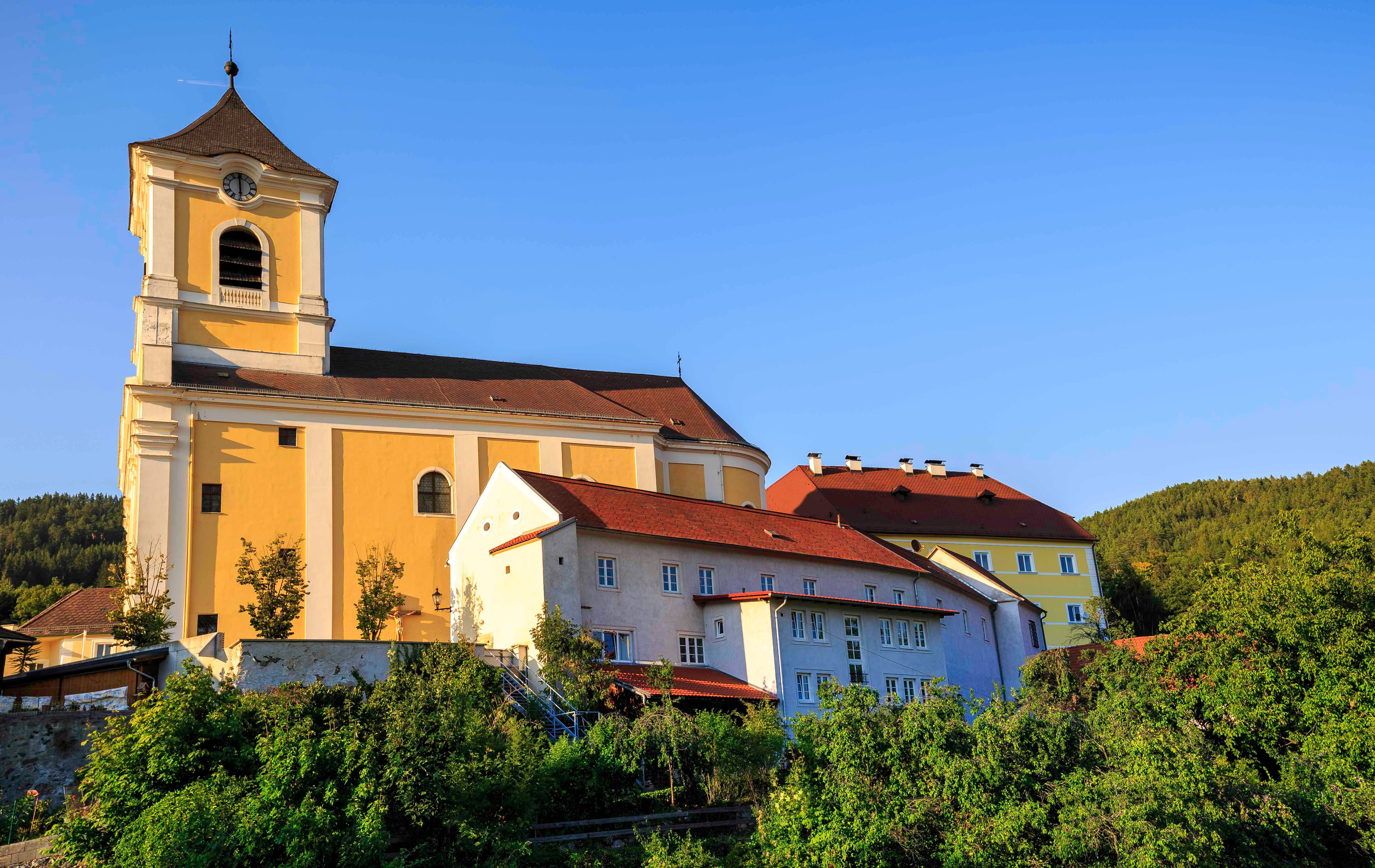 Pfarrkirche und Kloster in einer grünen Landschaft bei klarem Himmel.