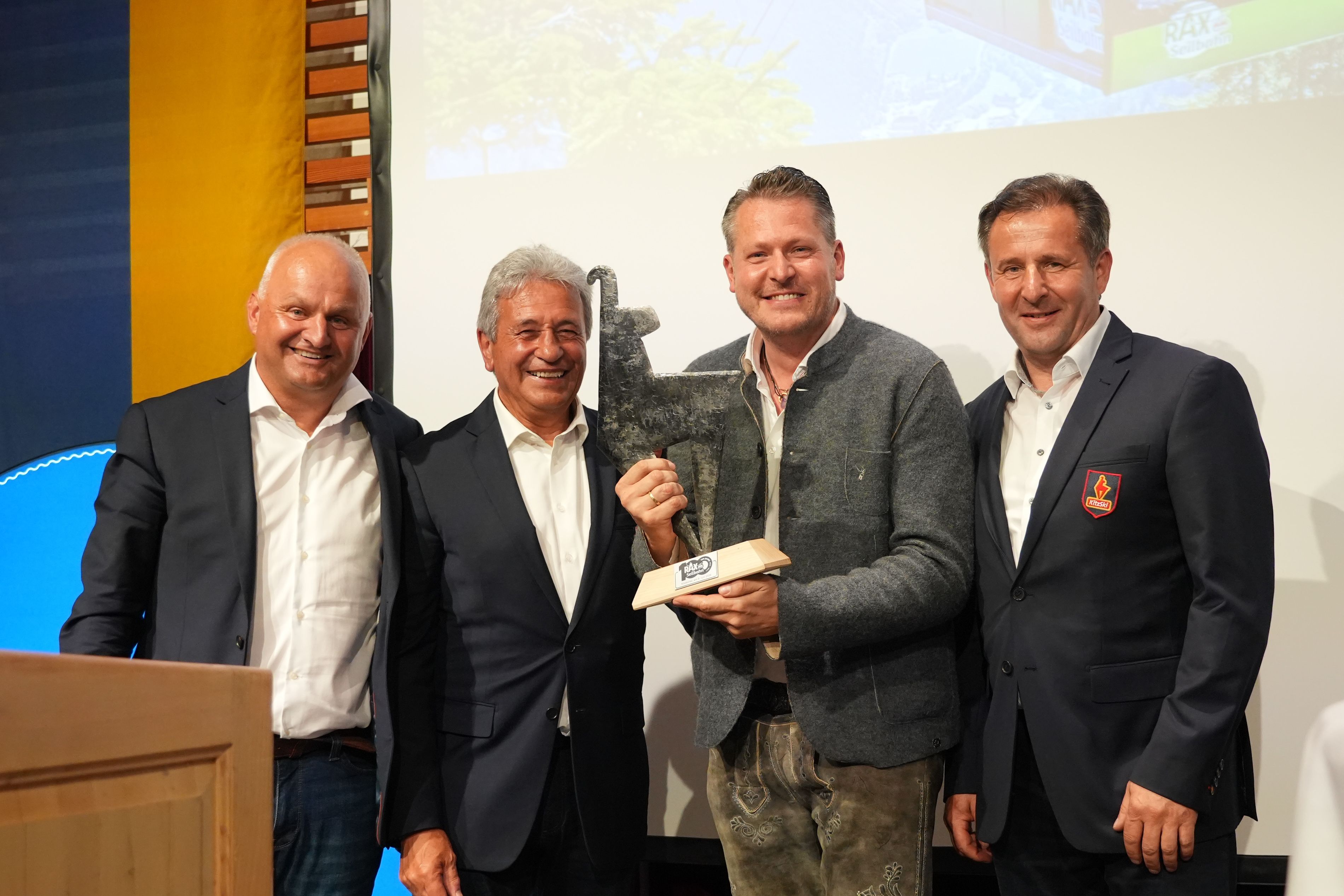 Vier Männer stehen auf einer Bühne und lächeln in die Kamera, ein Mann hält eine Trophäe, eine "Goldene Gams" in den Händen. 