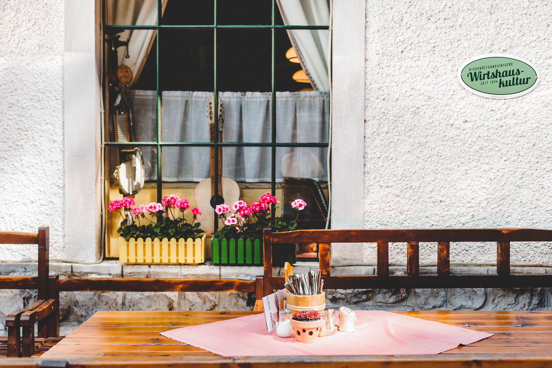 Im einladenden Gastgarten des Gasthauses Myrastubn blühen die Geranien in leuchtenden Farben und schaffen eine harmonische Atmosphäre. Die rustikalen Holzmöbel laden dazu ein, die frische Bergluft zu genießen und sich bei einem köstlichen Essen zu entspannen. Hier, umgeben von der Schönheit der Wiener Alpen, wird jeder Besuch zu einem unvergesslichen Erlebnis.
