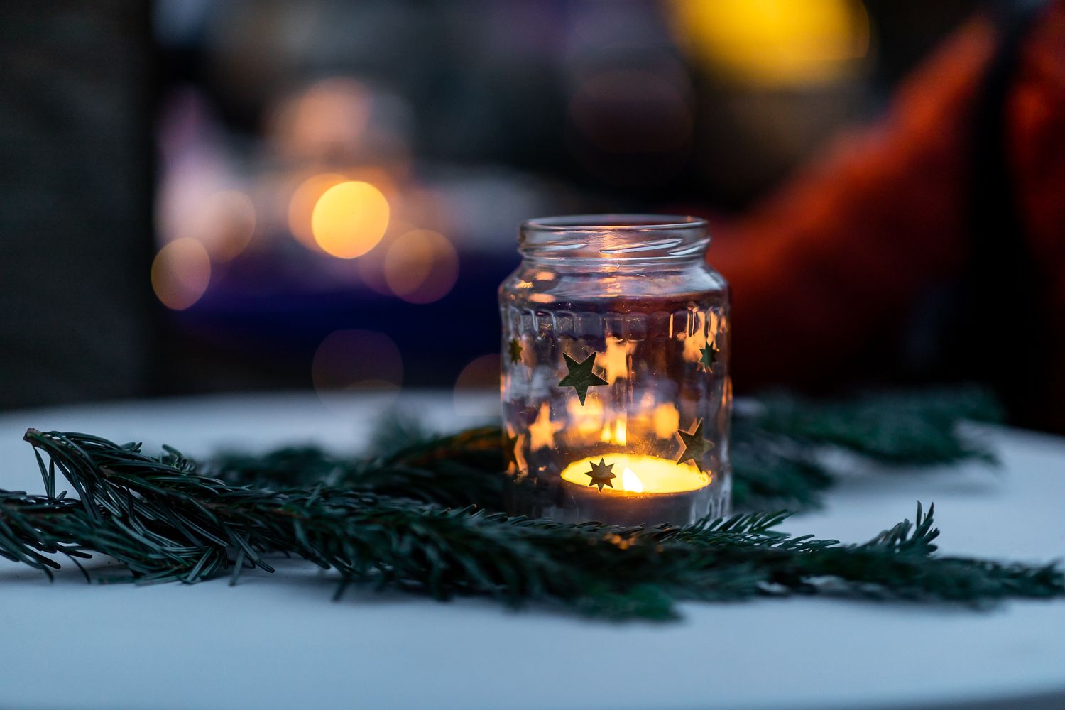 Tannenzweige und darauf steht ein Glas mit einem brennenden Teelicht