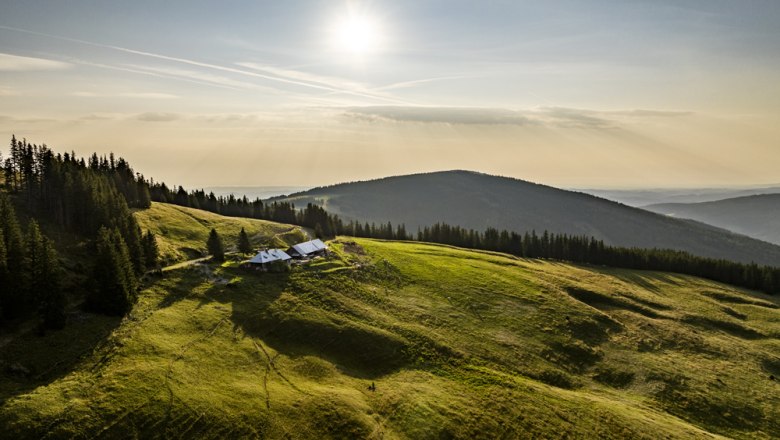 Landscape with green hills, forest and a building under the sun.