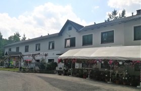 Ein zweistöckiges Gebäude mit der Aufschrift 'Waldpension', umgeben von Blumen und einem Vordach.