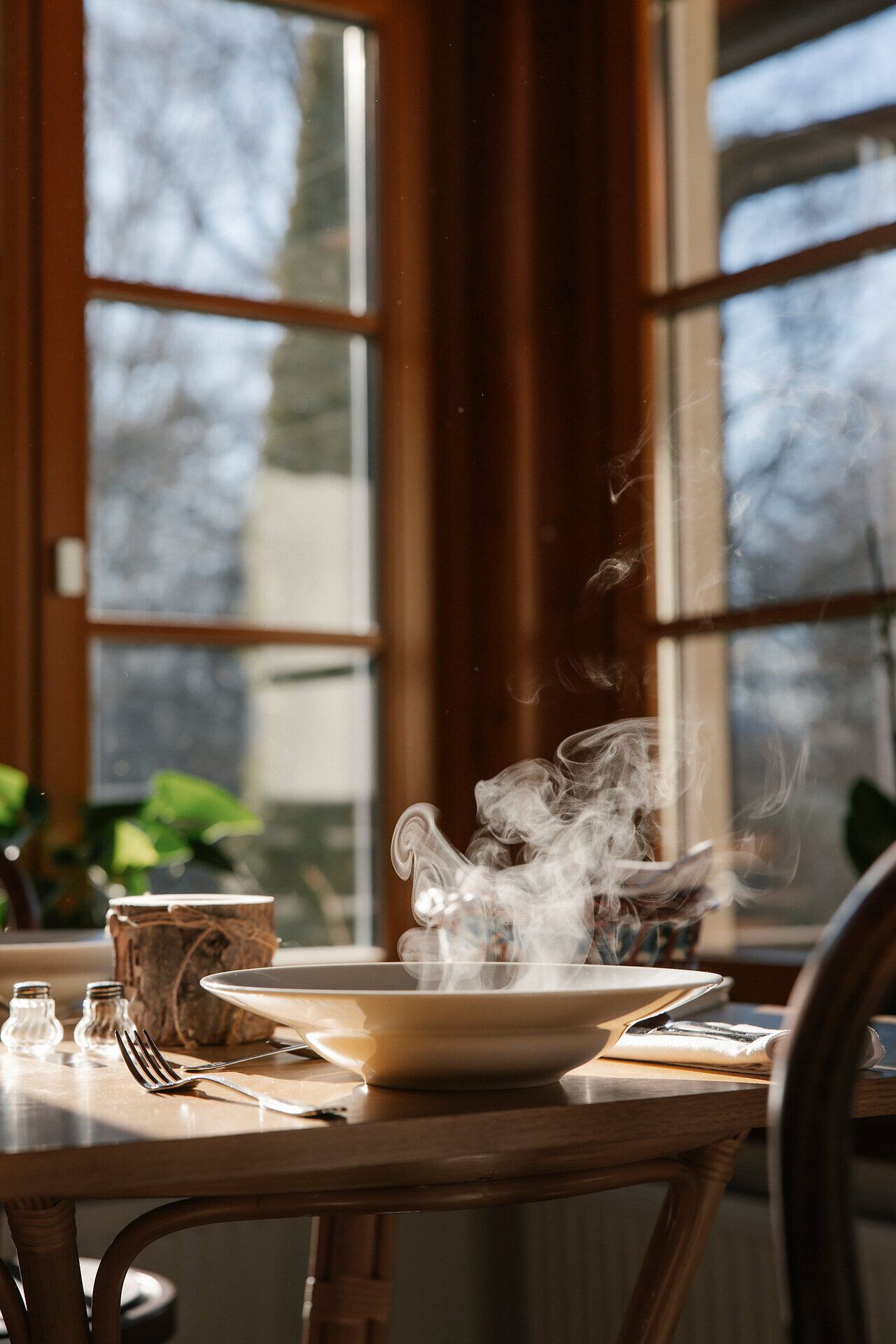 Dampfende Suppe auf einem gedeckten Tisch am Fenster.