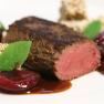 Gourmetgericht mit rosa gebratenem Fleisch, Obst und Kr&auml;utern auf einem wei&szlig;en Teller angerichtet.