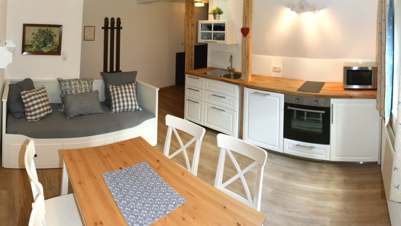 Gemütliche Küche mit Holztisch, weißen Stühlen, Sofa und moderner Küchenzeile.