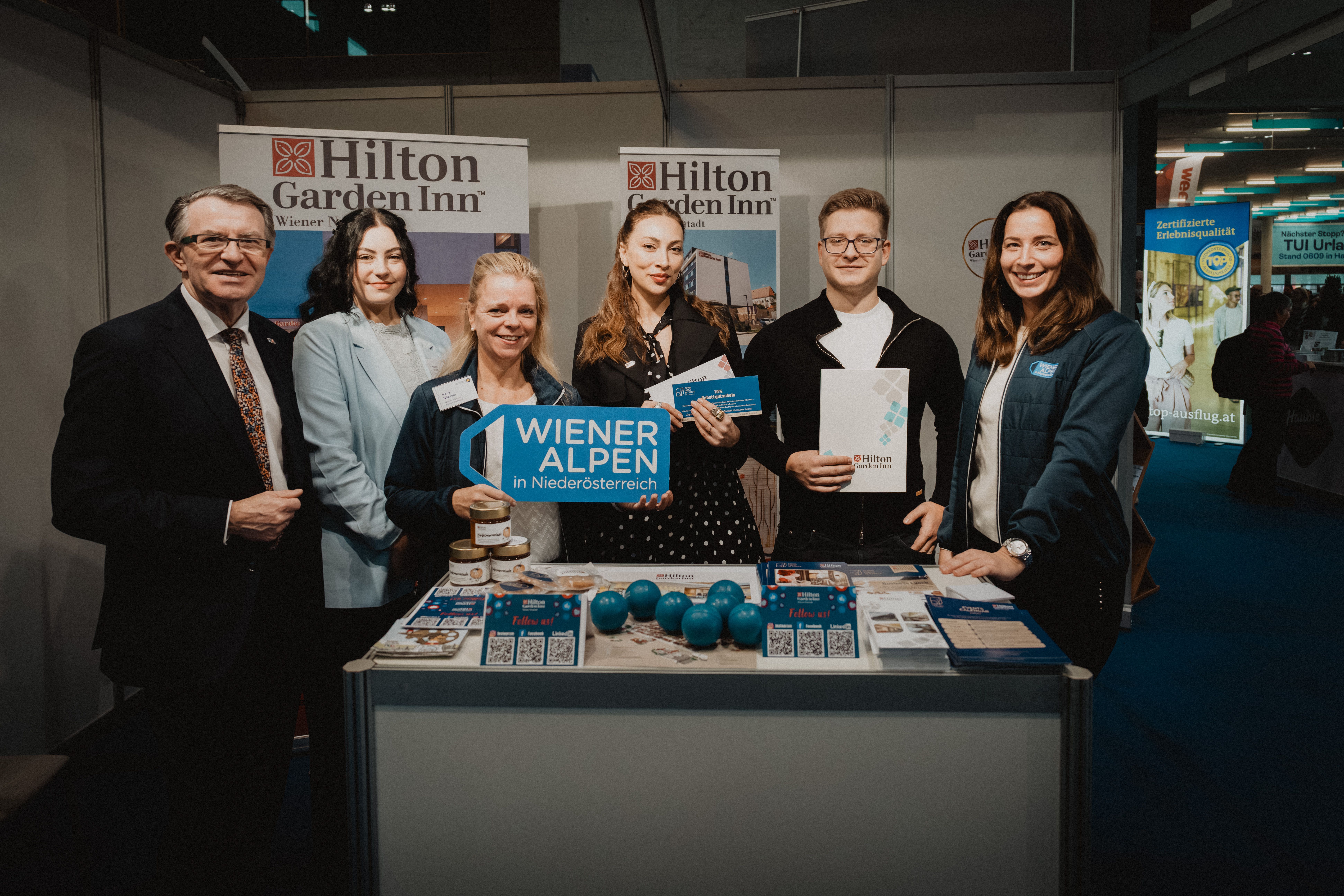 Sechs Personen mit dem Schild Wiener Alpen in Niederösterreich bei einem Prospektpult vom Hilton Garden Inn 
