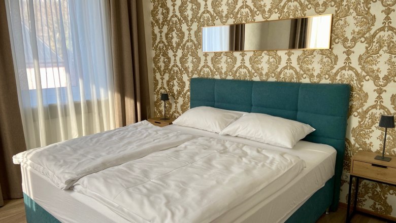 Ein stilvoll eingerichtetes Schlafzimmer mit einem gro&szlig;en Bett, blauen Kopfteil und goldener Tapete.