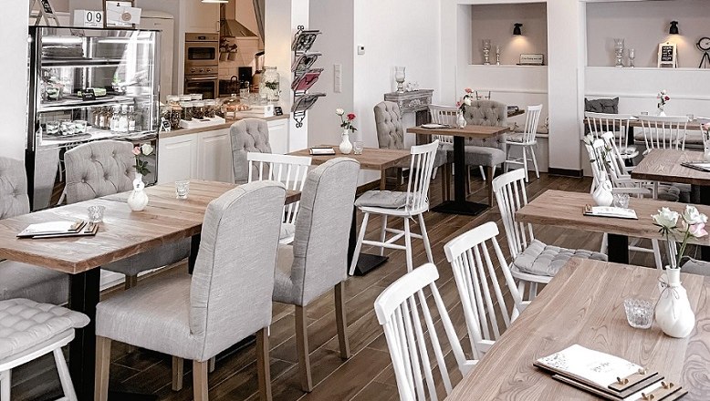 Innenansicht eines gemütlichen Cafés mit Holztischen und gepolsterten Stühlen.