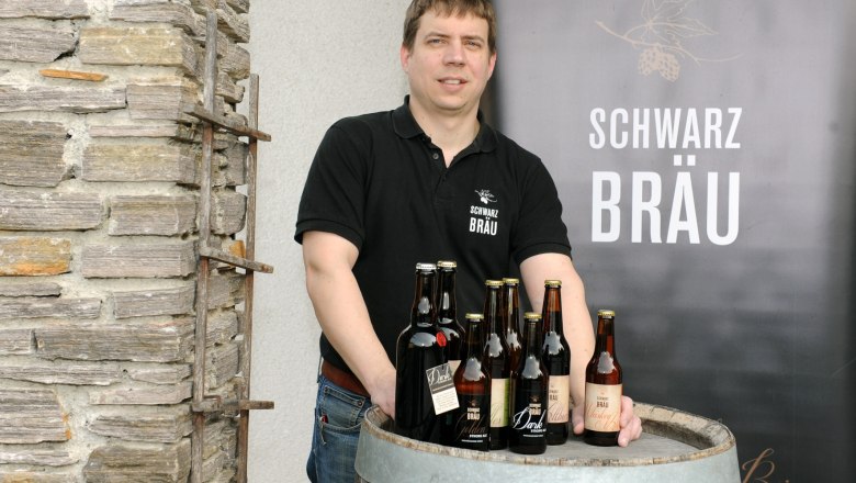 A man stands behind a wooden barrel with bottles of Schwarzbr&auml;u beer.