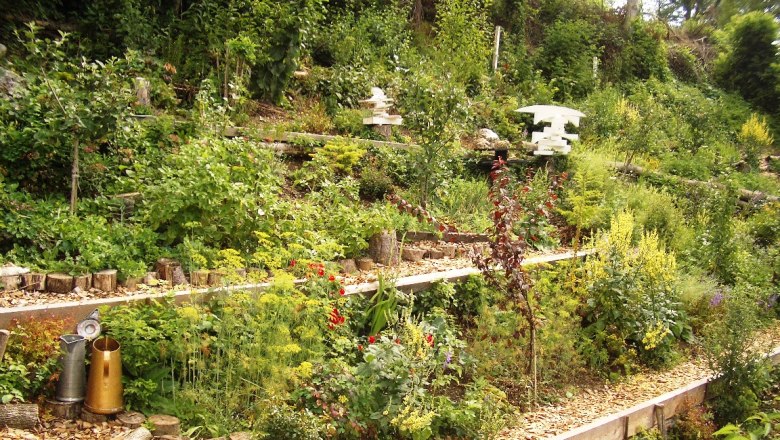 Terrassierter Garten mit üppiger Vegetation und dekorativen Elementen.