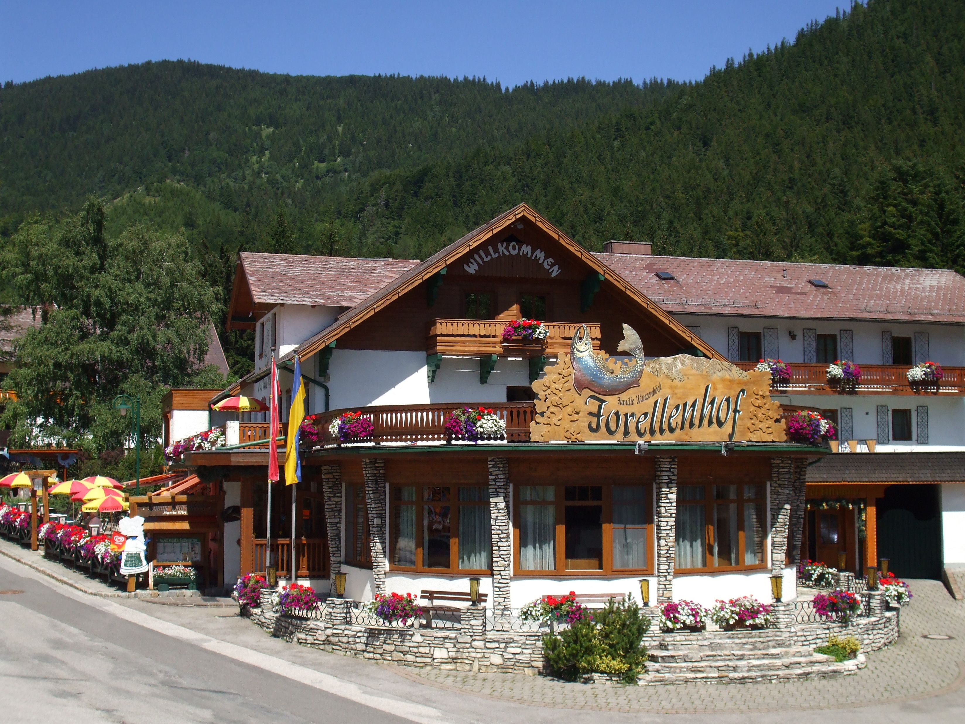 Familie auf sonniger Terrasse mit Bergen im Hintergrund, bedient von Kellnerin in traditioneller Kleidung.