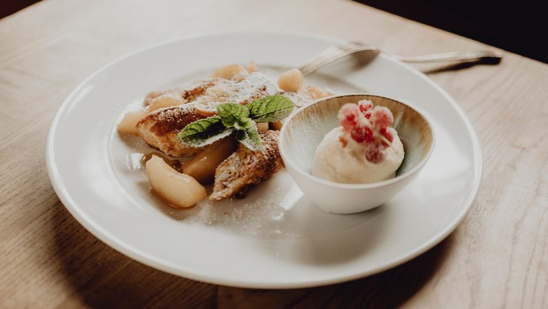 A plate of apple pancakes and a bowl of curd rum ice cream, garnished with mint leaves and red berries.