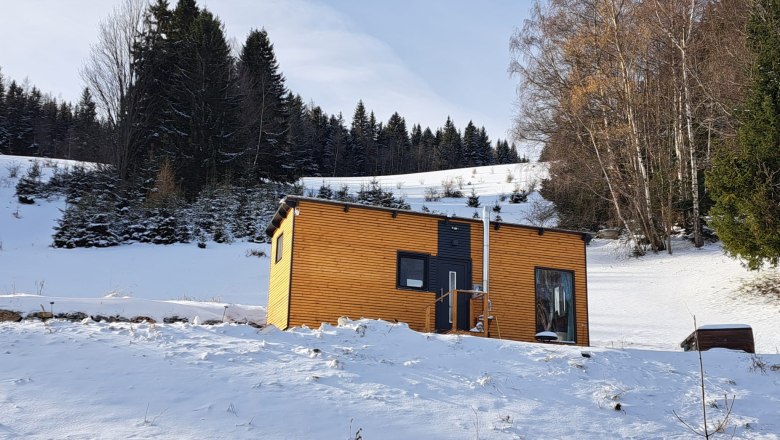 Small wooden house in the snow in front of a forest.