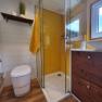 Modern bathroom with yellow shower screen, white WC, wooden shelf and window.