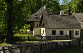 Ein traditionelles G&auml;stehaus mit Holzzaun und Garten, umgeben von B&auml;umen.