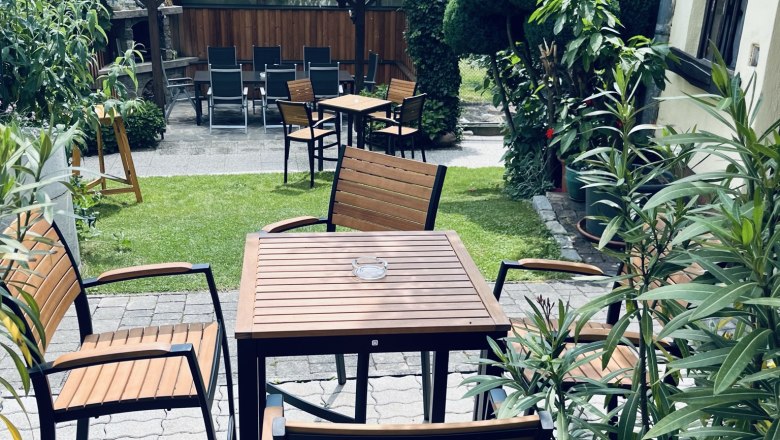 A cozy guest garden with wooden tables and chairs, surrounded by lush greenery and plants.