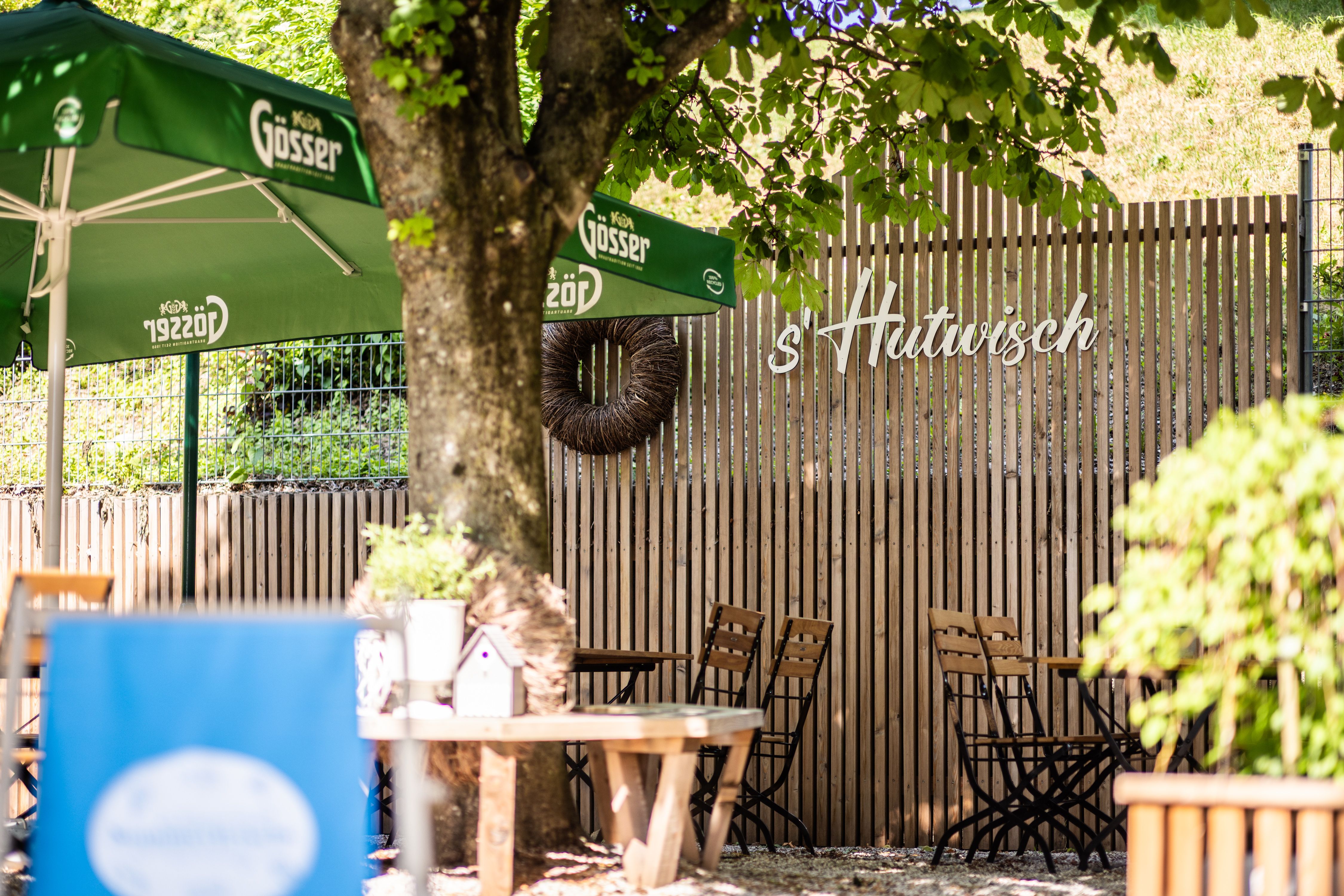 Ein sonniger Gastgarten mit Tischen, Stühlen und Sonnenschirmen. 