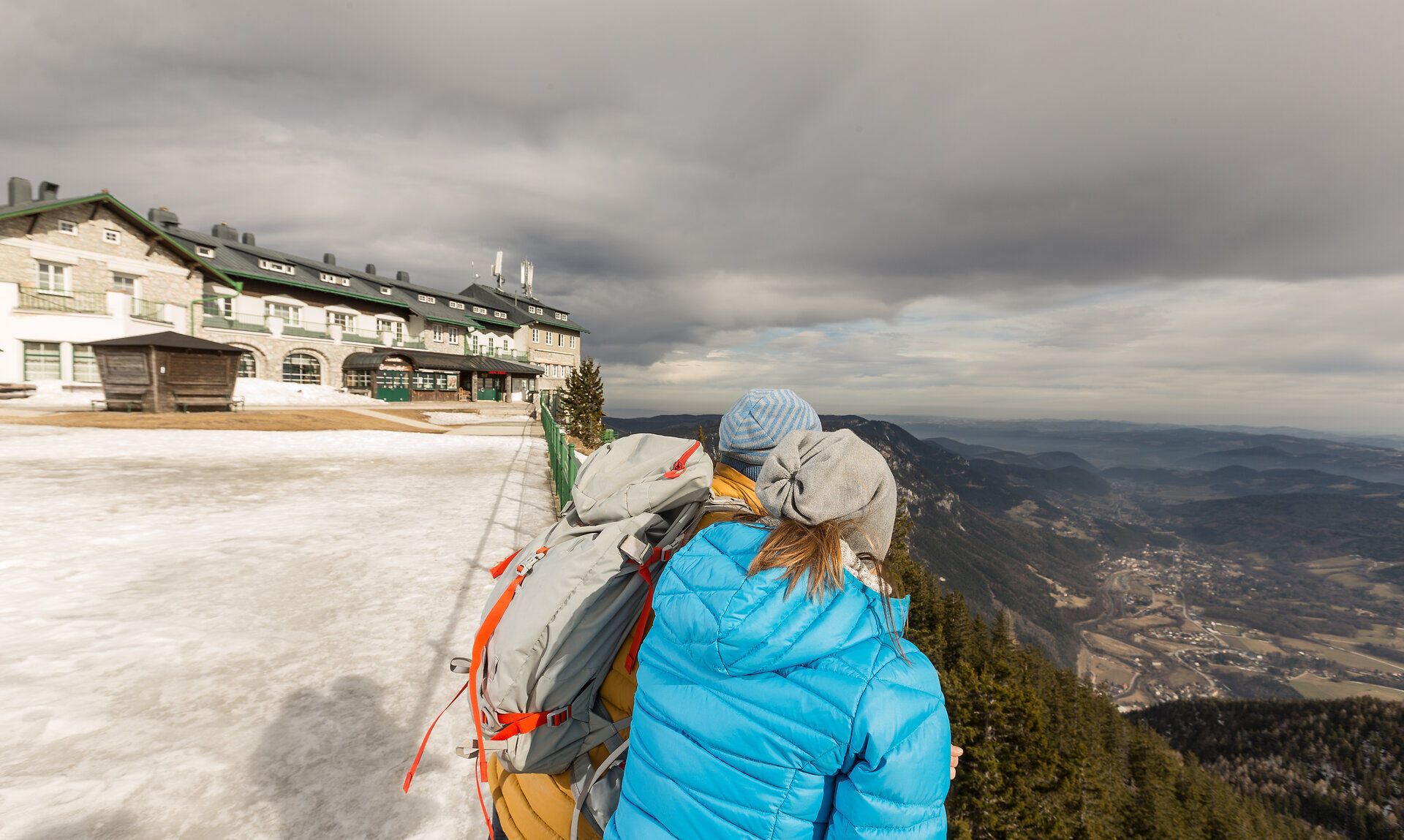 Die frische Bergluft umhüllt die Wanderer, während sie den atemberaubenden Ausblick auf die sanften Hügel und das weite Tal genießen. Die Wolken ziehen majestätisch über den Himmel und verleihen der Szenerie eine mystische Atmosphäre, die zum Verweilen einlädt.