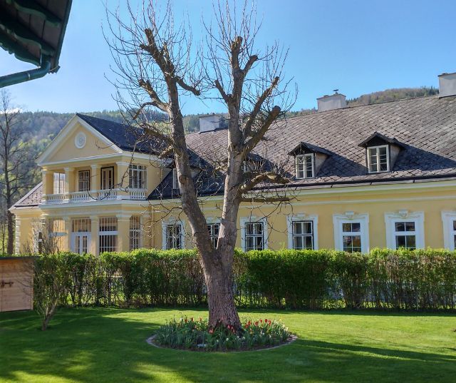 Gelbes Gebäude mit Balkon und Garten im Vordergrund.