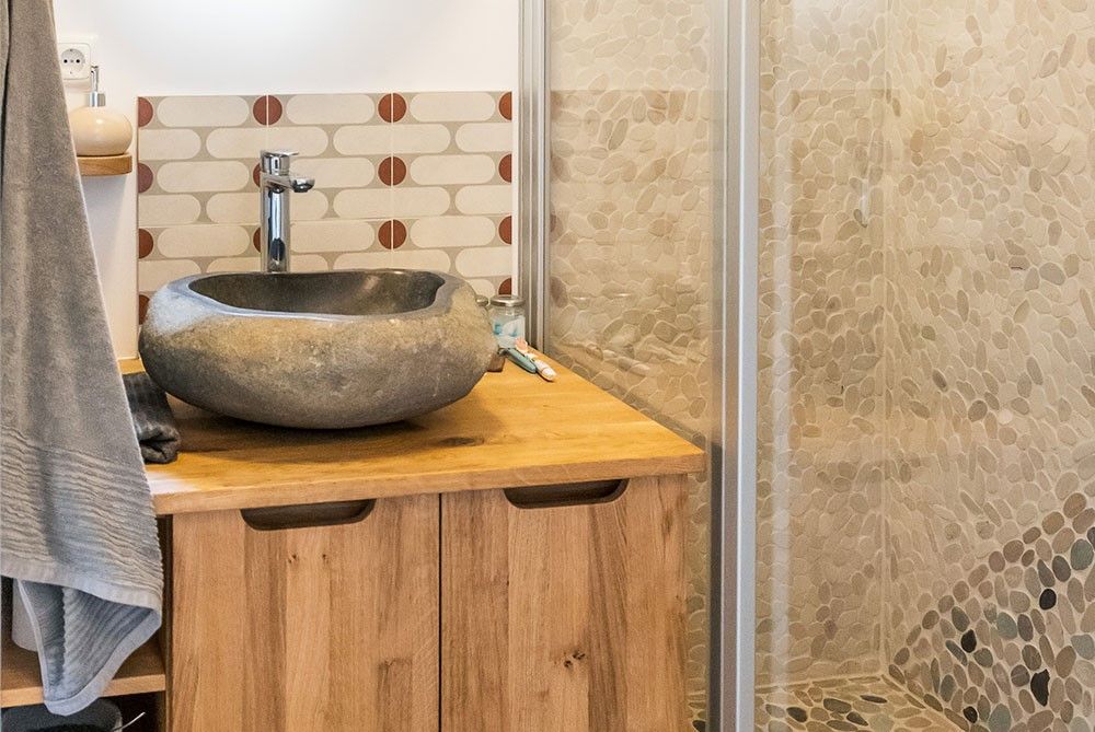 Modernes Badezimmer mit Natursteinwaschbecken und Holzschrank.