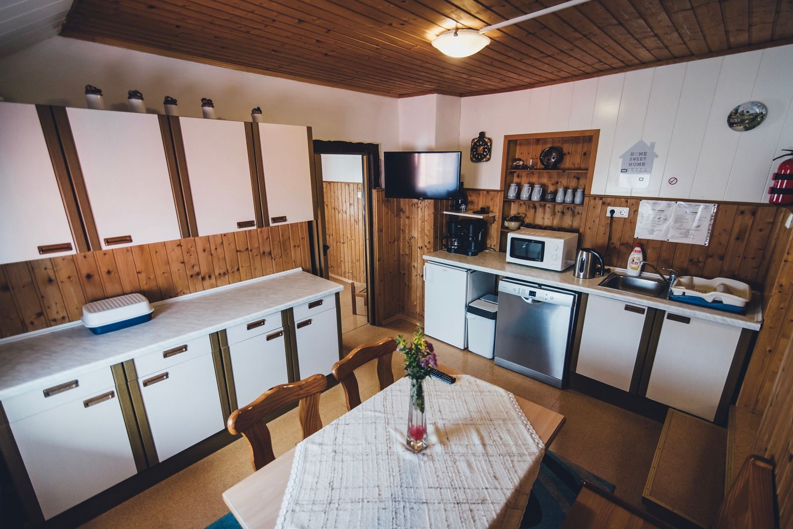 Gemütliche Küche mit Holzwänden, weißen Schränken, Esstisch und modernen Geräten wie Mikrowelle und Geschirrspüler.