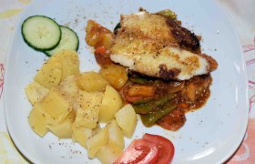 Ein Teller mit gebratenem Fisch, Kartoffeln, Gemüse und Gurken- sowie Tomatenscheiben.