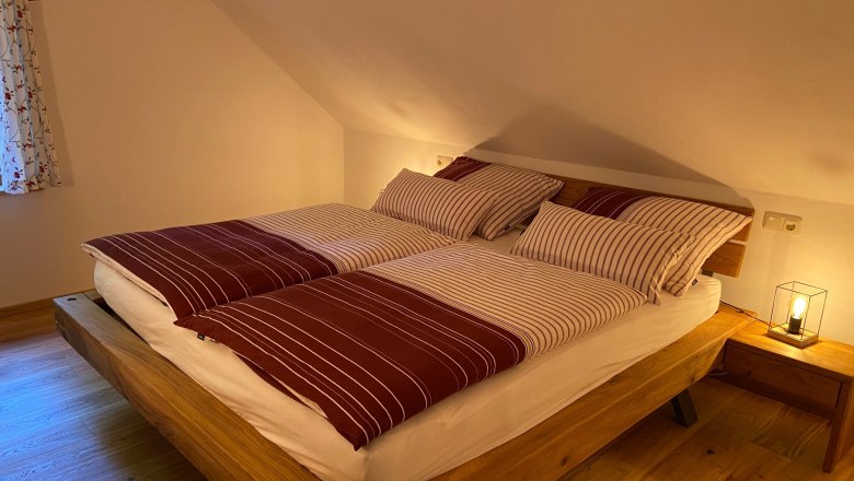 Gem&uuml;tliches Doppelzimmer mit Holzbett und gestreifter Bettw&auml;sche.