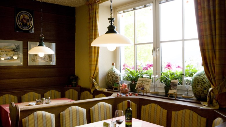 A cozy dining room with benches, tables, lamps and a large window with curtains.