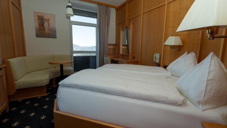 A cozy double room with wooden furniture, a double bed, a seating area and a balcony with mountain views.