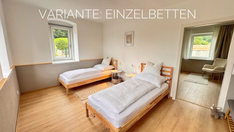 Schlafzimmer mit zwei Einzelbetten, Holzboden und Fenster mit Blick nach draußen.