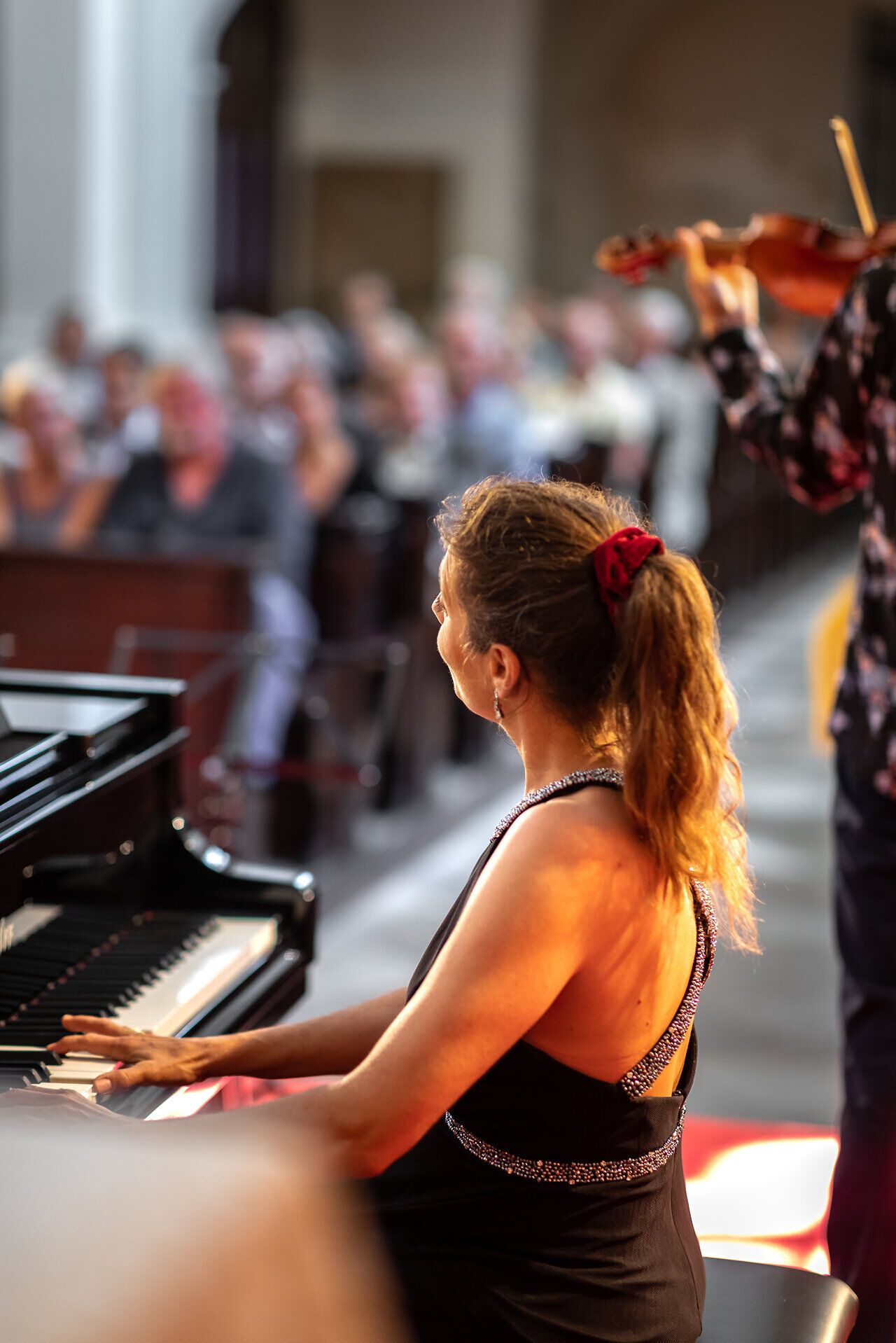 Eine elegant gekleidete Musikerin spielt auf dem Klavier vor einem Publikum in einer Kirche.