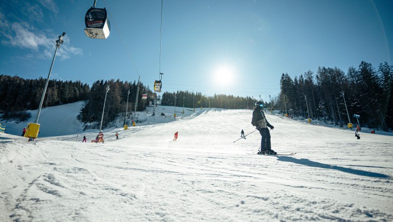 Skipiste am Semmering Hirschenkogel mit Skifahrern und Seilbahn bei Sonnenschein.