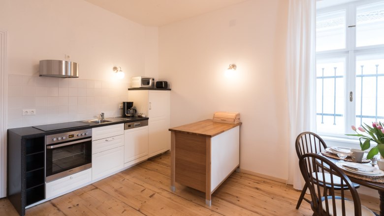 Moderne Küche mit Holzboden, weißer Einrichtung und kleinem Esstisch am Fenster.