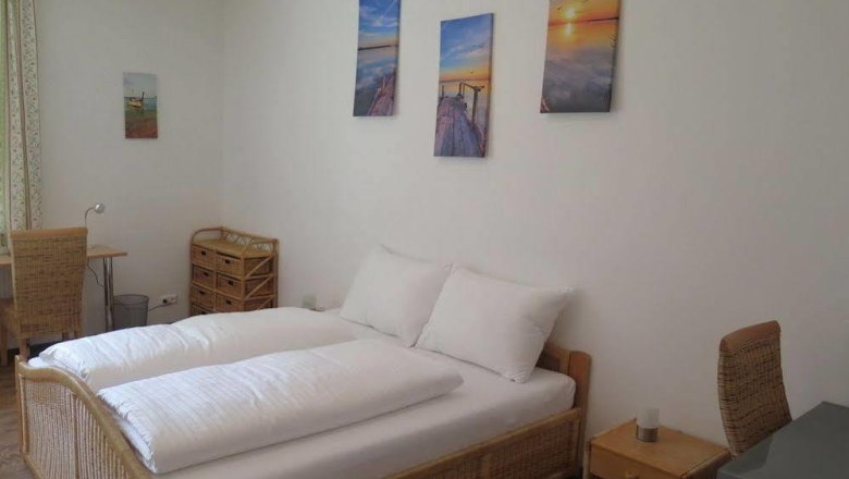 Helles Schlafzimmer mit Doppelbett, Rattanmöbeln und Wandbildern.