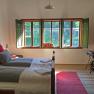 Cozy double room with wooden floor, bed, window with green shutters and a red carpet.