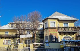 Gelbes Hotelgeb&auml;ude mit Holzverzierungen und blauen Himmel im Hintergrund.