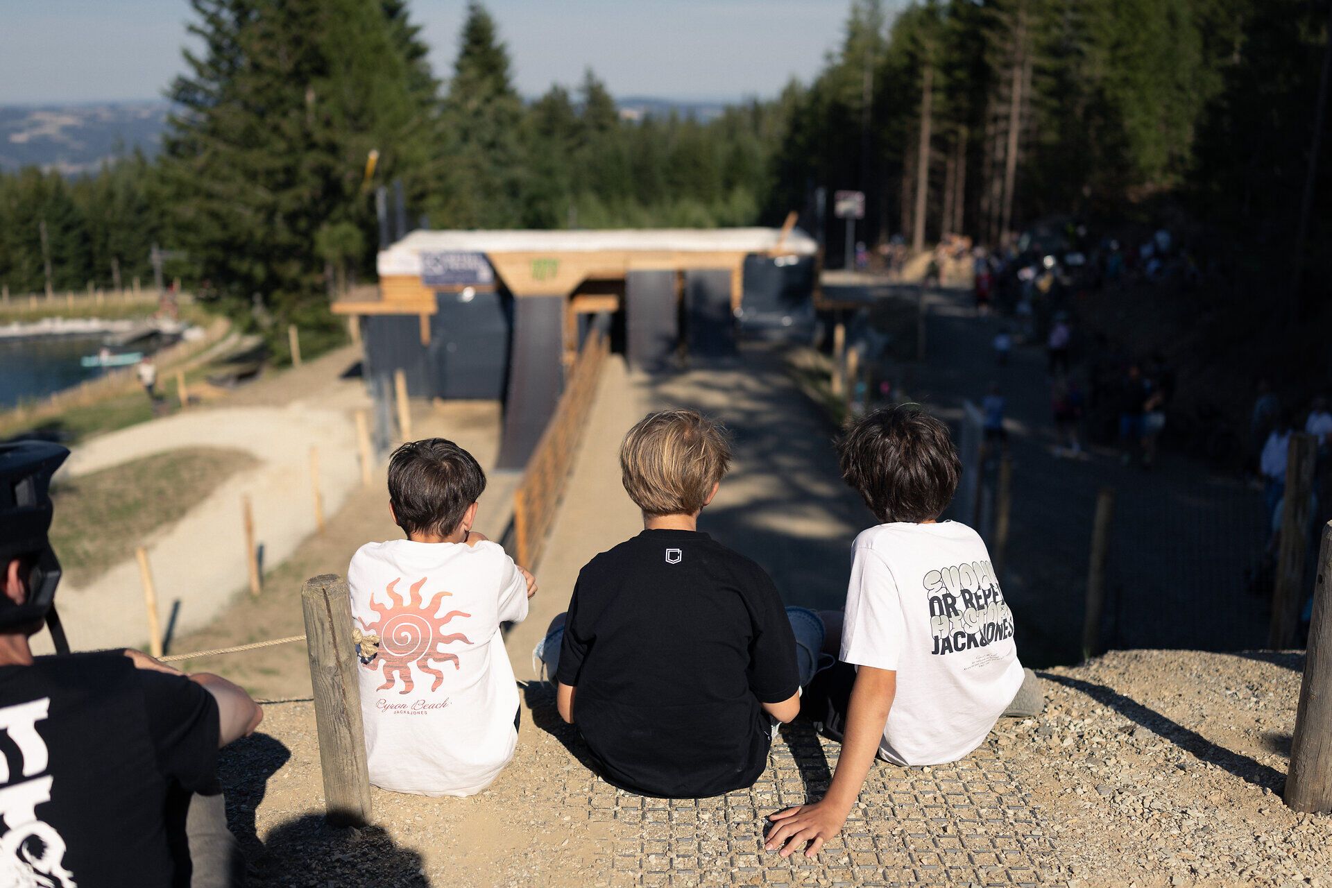 Drei Kinder beobachten den Wexl Freestyle Playground von einer Aussichtsplattform und verfolgen die Mountainbike-Sprünge auf der Strecke.