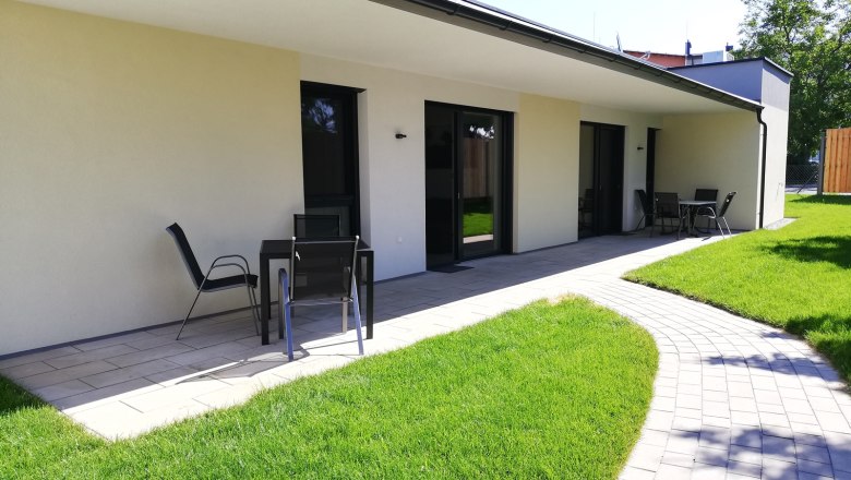 Terrace of a modern vacation bungalow with garden furniture and well-tended lawn.