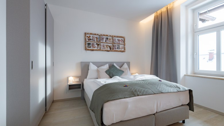 Modernes Schlafzimmer mit Doppelbett, grauen Vorhängen und Wanddekoration.