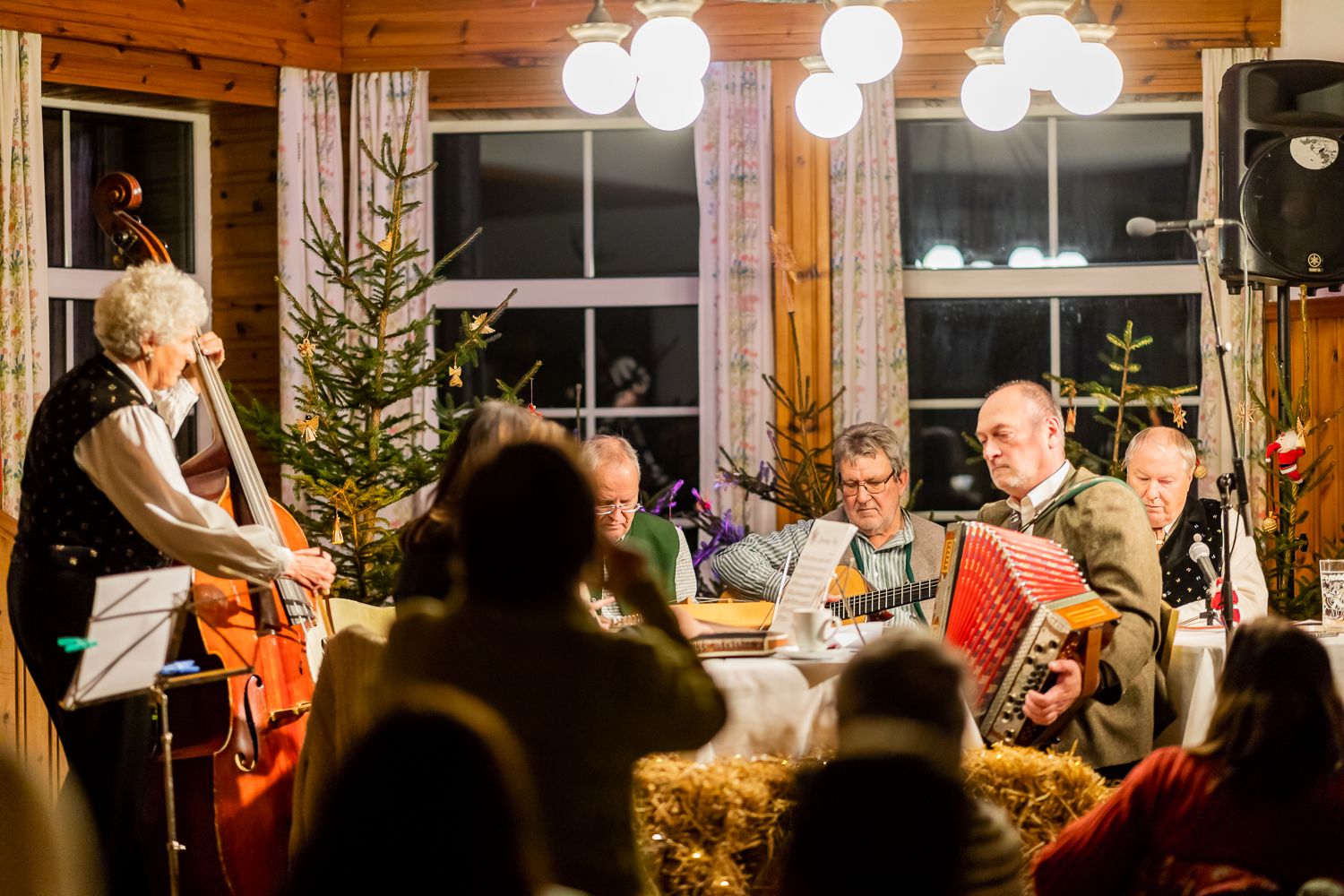 Musikanten sitzen rund um einen Holztisch in einer Hütte in weihnachtlichem Ambiente