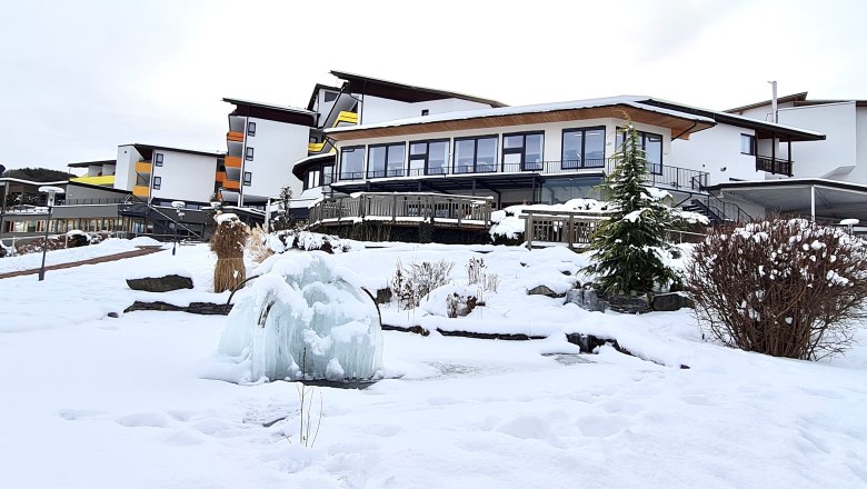 Verschneites Hotelgebäude mit gefrorenem Brunnen im Vordergrund.