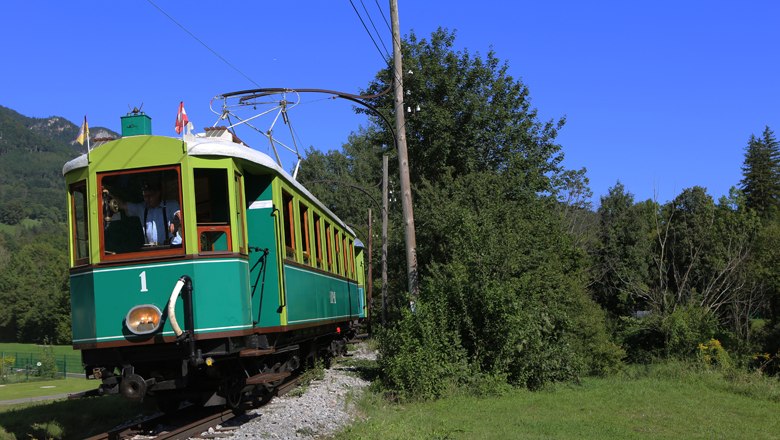 Historische grüne Bahn fährt durch eine grüne Landschaft unter blauem Himmel.