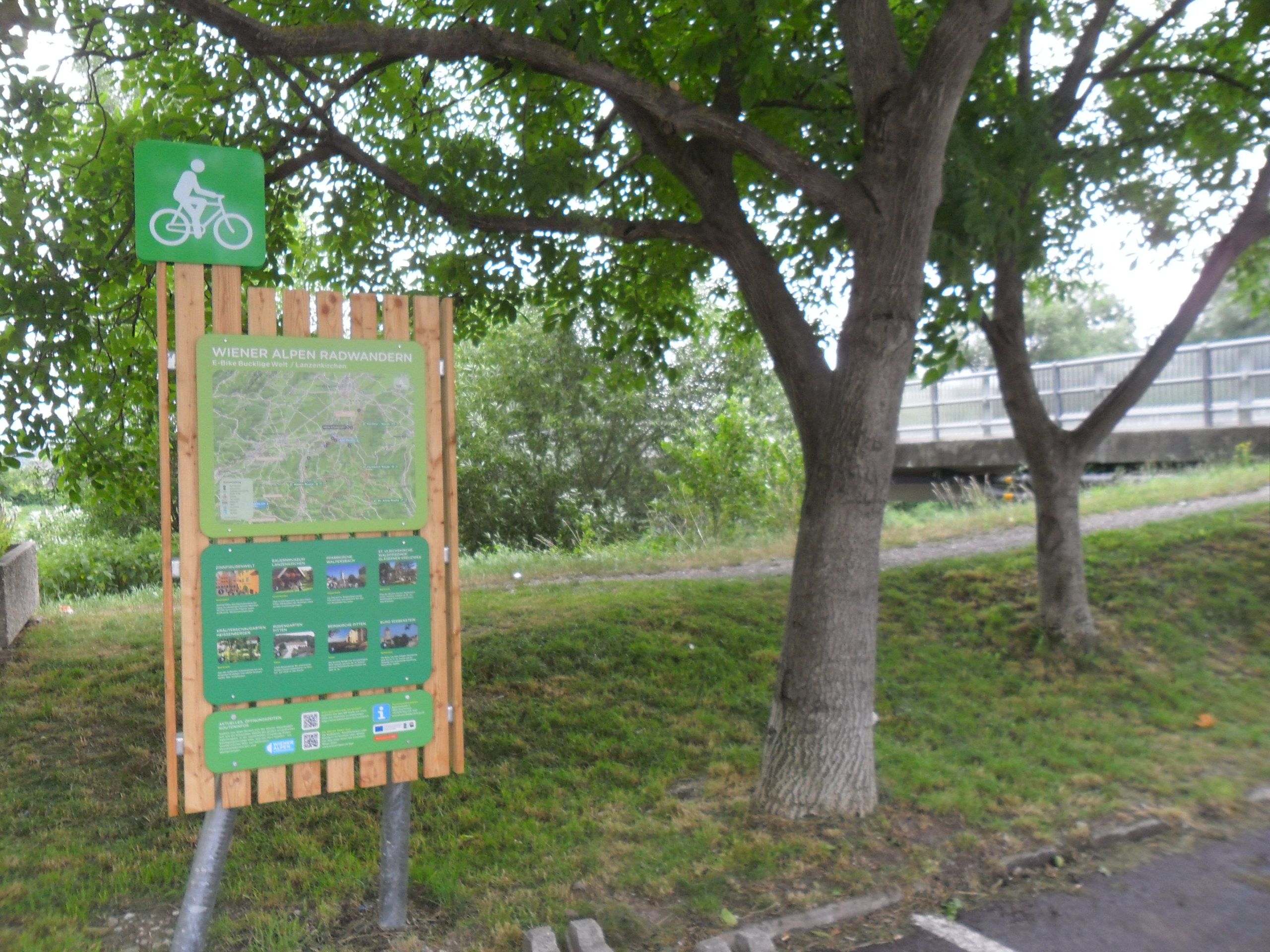 Radstartplatz-Tafel in Lanzenkirchen mit Karte und Informationen, umgeben von Bäumen.