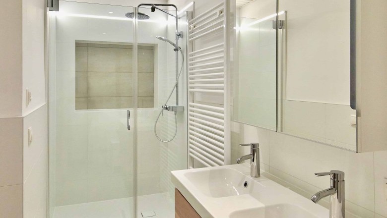 Modern bathroom with double washbasin, glass shower and towel radiator.